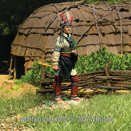 Collectible toy soldier wearing Native American clothing standing in front of a hut.