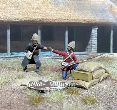 Two toy soldiers in historical military uniforms, one kneeling with a rifle and the other standing with a gesture, are set outside a thatched-roof building. Nearby, sandbags and a shield complete this classic toy solider scene.