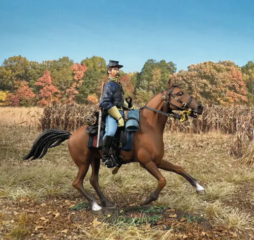 The W.Britain Union Cavalry Trooper Mounted on Trotting Horse, No.2 features a toy soldier in blue uniform riding a brown horse across an autumn field, capturing historical elegance beneath a clear blue sky.