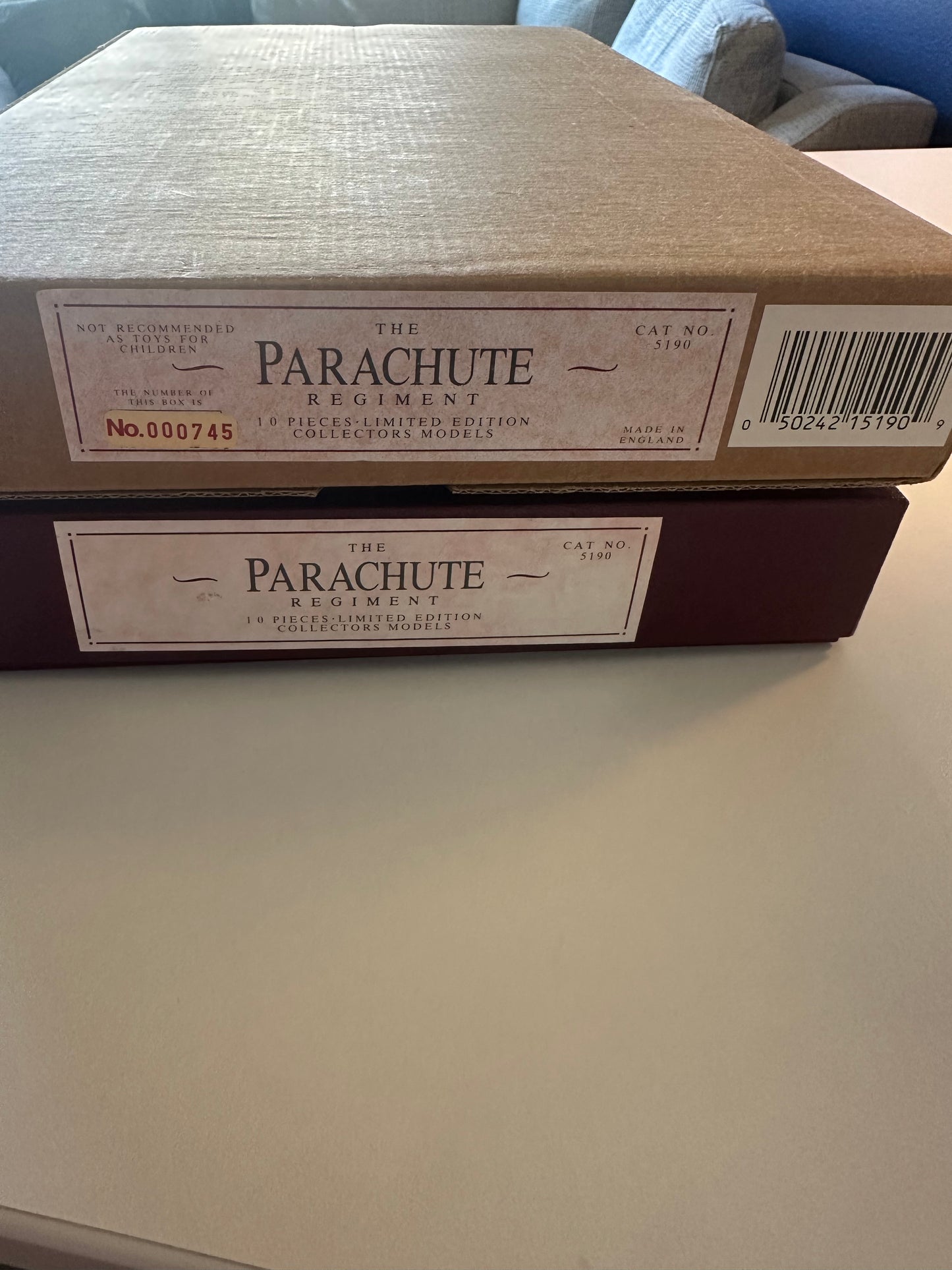 Shipping box for A display box containing ten miniature toy soldiers and a white animal figure, representing The Parachute Regiment. Each soldier holds different flags or items, arranged neatly in a blue velvet-lined box with a description label on the lid.