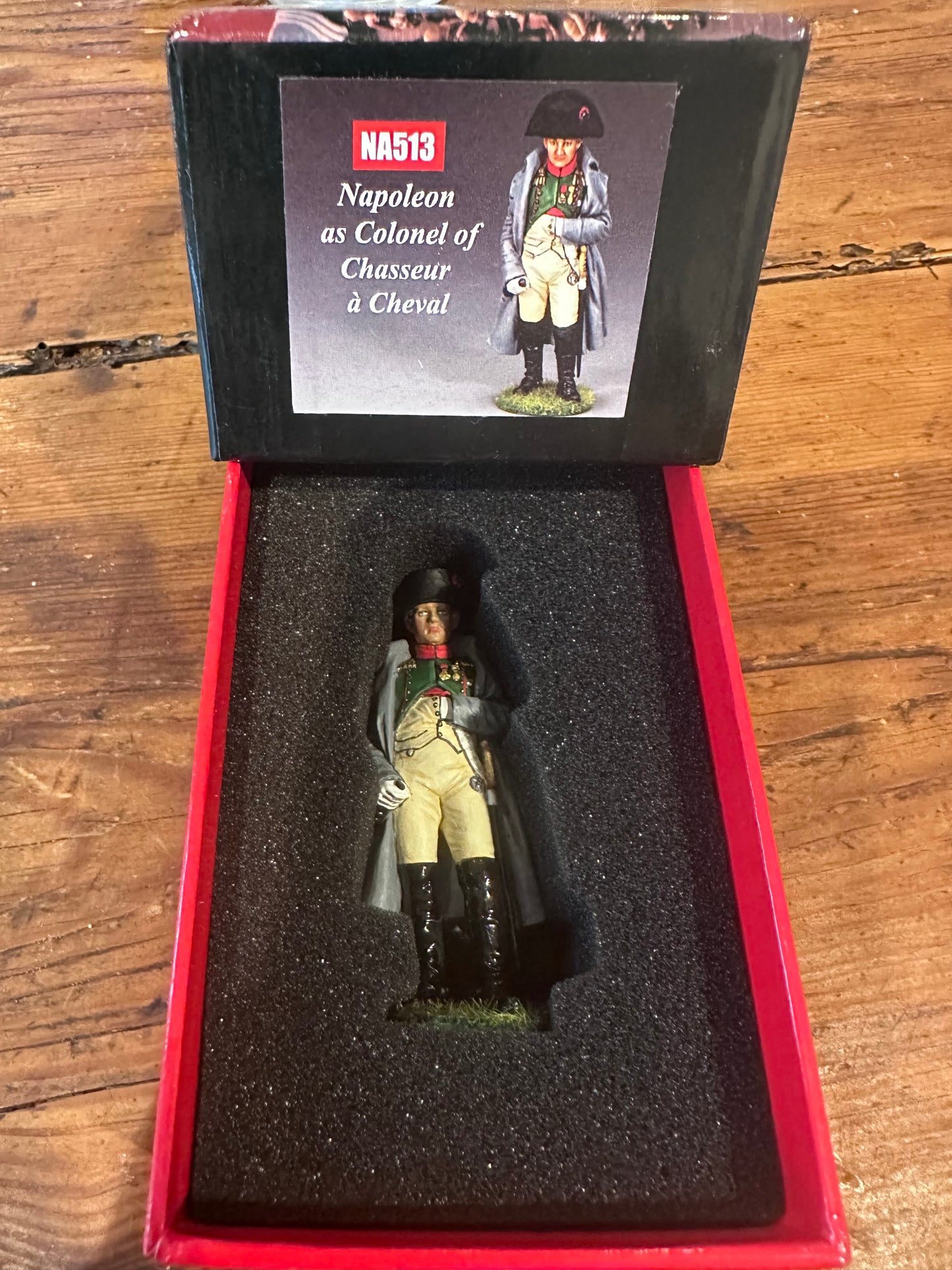 Model figure of a Napoleon in a display case with a label on a wooden surface