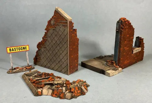 Miniature diorama scenery depicting war-torn ruins: a damaged brick wall, debris, a section of broken building, and a small sign that reads Bastogne, with space to add toy soldiers, all set against a plain background.