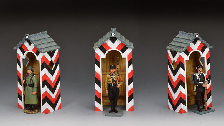 Three model figures in front of decorative sentry boxes with red, black, and white patterns on a gray background.