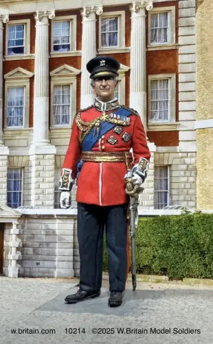 King Charles III by W. Britain — 1/30 scale matte-painted figure in red British military dress uniform with blue sash, peaked cap, and ceremonial sword. Catalog 10214.