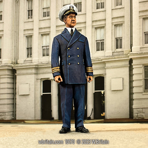 A toy soldier figurine of U.S.N. Commander Richard Nixon dressed in a dark navy blue military uniform with double-breasted jacket and gold cuff rings, standing in front of a classical building facade. Nixon is depicted with a stern expression, wearing a naval cap and holding his hands clasped in front. The figure is highly detailed, capturing the essence of his naval service, set against a realistic backdrop suggestive of his later political career.