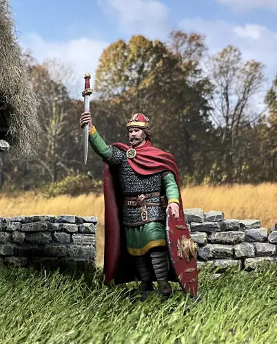 Collectible toy soldier military miniature figurine A detailed miniature of a medieval knight in armor holds a sword upright and a round shield. The knight, with a red cape, crown-like helmet, and beard, stands on a textured base.