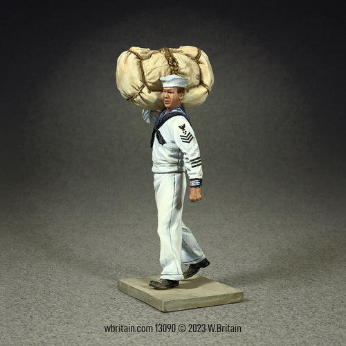 Miniature figurine of a U.S.N. sailor in a white service uniform, walking with a seabag and hammock over his shoulder.