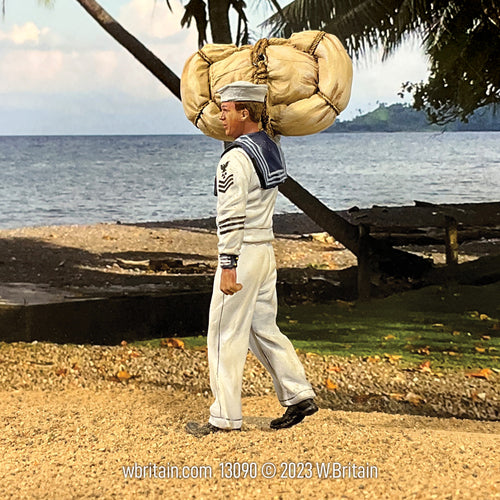 Miniature figurine of a U.S.N. sailor in a white service uniform, walking with a seabag and hammock over his shoulder. The sailor wears a 'Dixie Cup' hat and a V-neck jumper with a squared 'sailor collar'. The background features a coastal scene with a sandy beach, palm trees, and the sea, evoking a summer-friendly atmosphere appropriate for the 'undress whites' uniform.