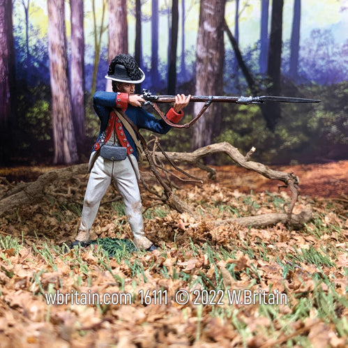 Collectible toy soldier miniature in white pants and blue jacket. Soldier is aiming musket with forest in background. 