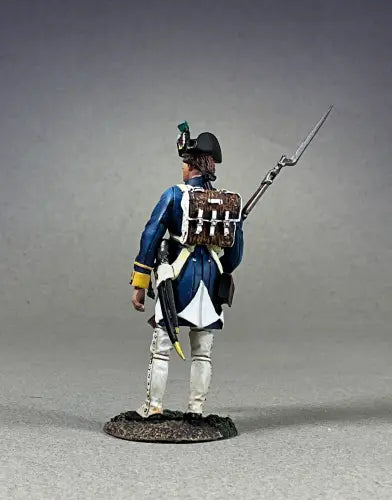 Rear view of A toy soldier figurine of a Revolutionary War-era soldier in a blue coat with yellow trim, white pants, and a black tricorne hat, holding a musket with bayonet and standing on a textured base.
