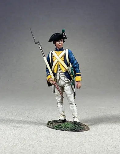 A toy soldier figurine of a Revolutionary War-era soldier in a blue coat with yellow trim, white pants, and a black tricorne hat, holding a musket with bayonet and standing on a textured base.