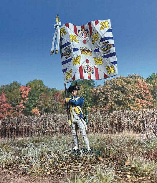  A collectible toy soldier figurine of a historical soldier in a blue uniform holding a large flag with white and purple stripes, yellow fleurs-de-lis, and ornate circular designs. The soldier stands on a grassy base. He is on the field of battle.