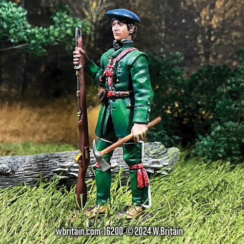 Miniature figurine of a Rogers' Rangers Private from 1758, standing in a naturalistic setting. The soldier is dressed in a vibrant green uniform with red trim and carries a musket. He also has a hatchet hanging from his belt and a black tricorn hat, highlighting his readiness for both combat and survival tactics used during the French and Indian War.