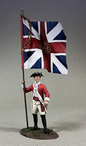 A toy soldier figurine in an 18th-century British red uniform holds a large British flag with a royal emblem, standing on a textured base against a plain background.