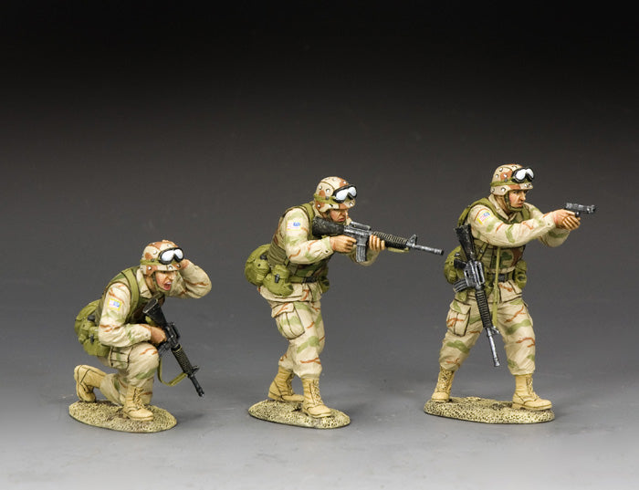 Three toy soldier U.S. Army Rangers in desert camo: one fires a pistol, one advances with M16A2, and one kneels adjusting helmet under fire.