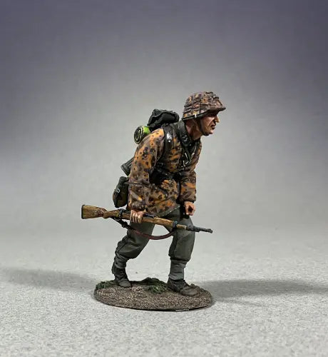 Side view of A toy soldier figurine, dressed in a detailed camouflage uniform and helmet, crouches while gripping a rifle. With gear strapped to his back, he is poised on a small textured base against a plain gray backdrop.