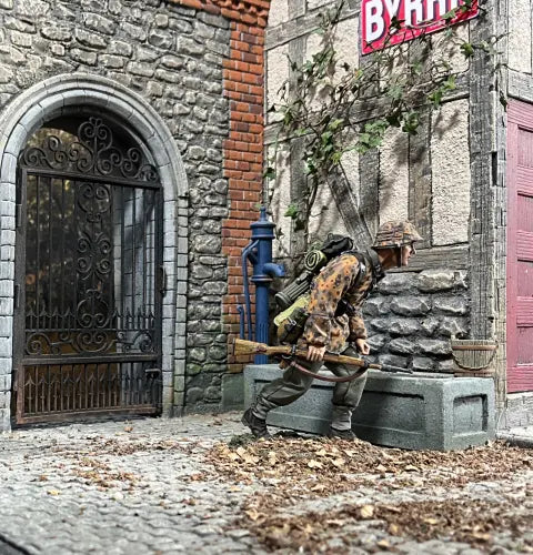 Urban combat of A toy soldier figurine, dressed in a detailed camouflage uniform and helmet, crouches while gripping a rifle. With gear strapped to his back, he is poised on a small textured base against a plain gray backdrop.