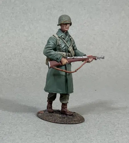 A miniature toy soldier from World War II stands on a small base, dressed in a green coat, helmet, and clutching a rifle. This intricate figurine features detailed accessories like a belt and boots, all set against a neutral background.