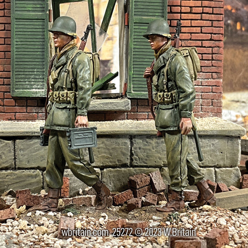 A highly detailed 1/30 scale toy soldier set depicting two U.S. Infantrymen from World War II, marching past a war-damaged building.