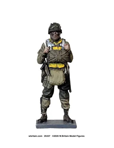A painted military model figure of a soldier in combat gear, standing on a dark display base against a plain white background. The figure is wearing a helmet, tactical vest, and boots, with yellow accents on the chest.