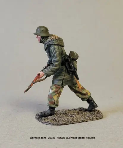 A painted miniature model of a World War II German soldier in winter camouflage, posed in a marching stance on a textured base. The figure is wearing a green helmet, a winter jacket with a fur collar, and camouflage trousers, holding a rifle.
