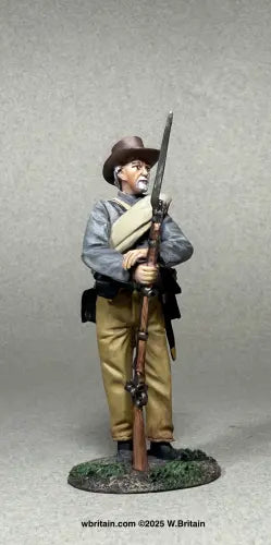 Confederate Infantry at Rest. A detailed figurine of an older Civil War soldier in a brown hat, gray jacket, and tan pants stands holding a rifle with a bayonet attached, against a plain backdrop. The base is grassy terrain.