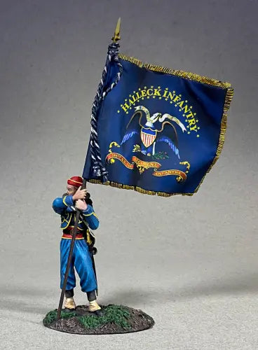 A figurine of a historical soldier holding a flag. The soldier is dressed in a blue and red uniform with gold accents. The flag is blue with an eagle and stars, and says Halleck Infantry. The figurine stands on a small grassy base.