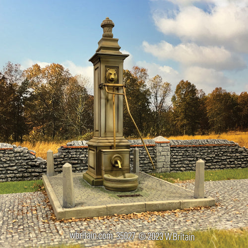 A detailed miniature model of a 19th-century village pump, set within a scenic backdrop featuring autumn trees and stone walls. 