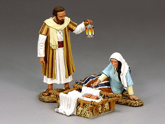 Two figurines in a nativity scene setting with one holding a lantern.