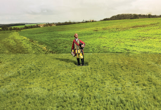 Large green field with 54mm toy soldier figurine in red coat and yellow pants.