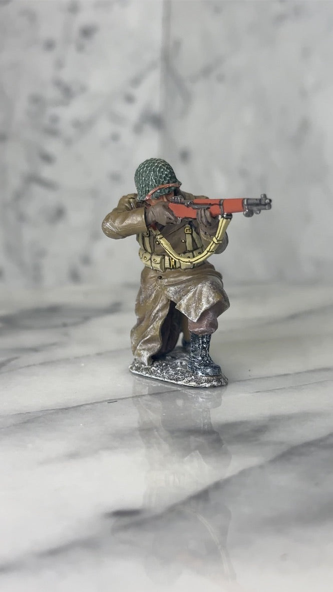 360 view of King & Country BBA094 figure of a U.S. infantryman kneeling in the snow in a long winter overcoat, aiming his M1 Garand rifle. White marble background.