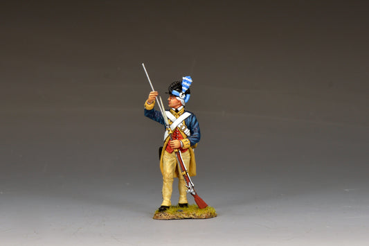 A detailed figurine of an 18th-century soldier in a blue and yellow uniform, holding a rifle upright with one hand and saluting with the other, stands on a small grassy base against a plain background.