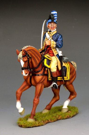A painted military miniature figurine of a soldier in an 18th-century uniform riding a brown horse with a white mane and tail, set on a grassy base. The soldier holds a sword and wears a blue jacket with yellow trim.