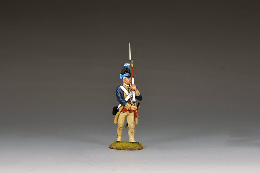 A painted miniature figurine of a Revolutionary War soldier in blue and tan uniform holding a musket upright, standing on a small patch of grass against a plain gray background.