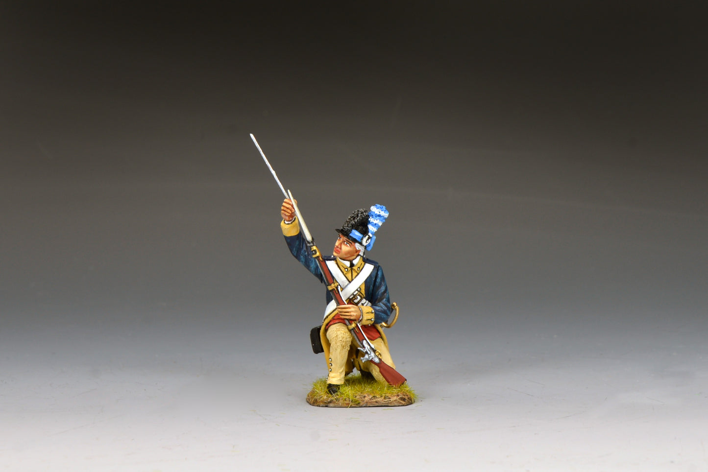 Kneeling Washington’s Guard soldier using a ramrod to reload his musket, wearing blue coat and tricorn with plume.