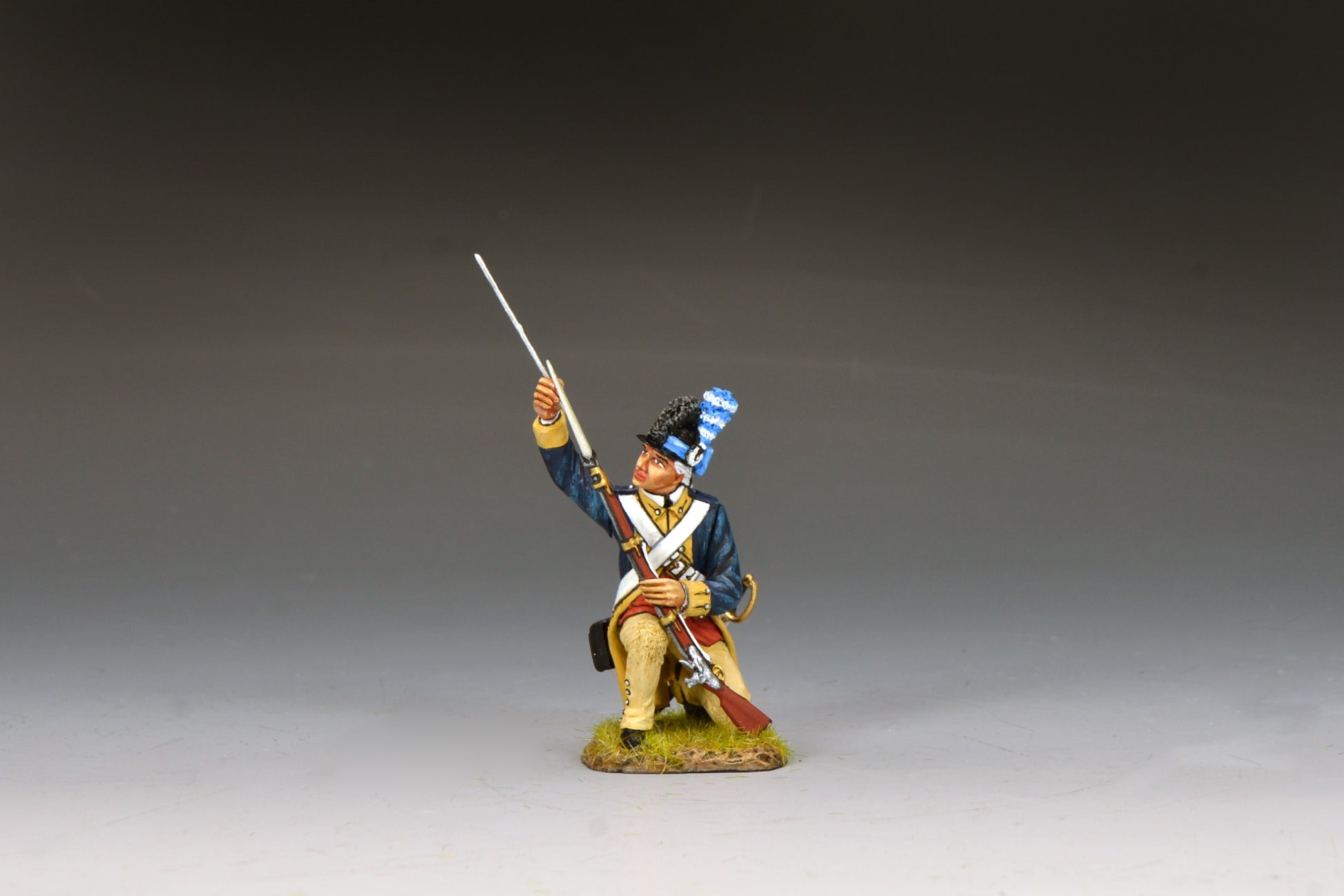 Kneeling Washington’s Guard soldier using a ramrod to reload his musket, wearing blue coat and tricorn with plume.
