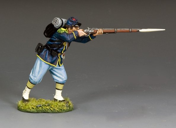 Military miniature Union soldier advances while firing his musket, leaning forward with bayonet fixed and full campaign gear on his back.