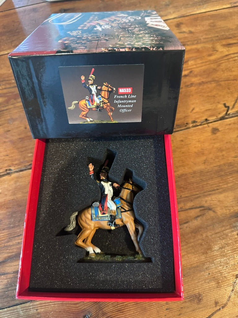 A miniature French Equestrian Officer figurine NA533 displayed inside its open red and black presentation box on a wooden table. The figurine depicts a soldier in a black coat and hat riding a light brown horse, set against a black foam insert.