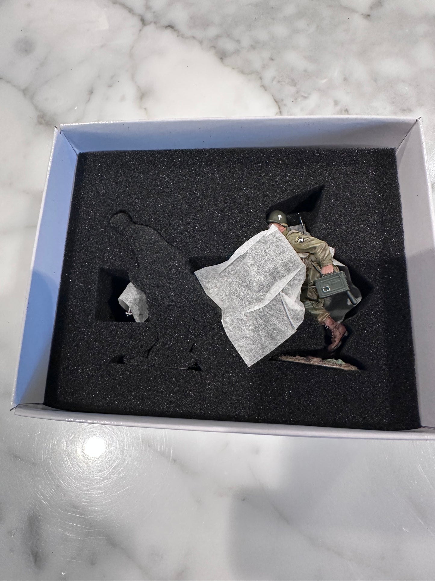 Toy Soldier figurine of a person in a suit inside a shadow box on a marble surface