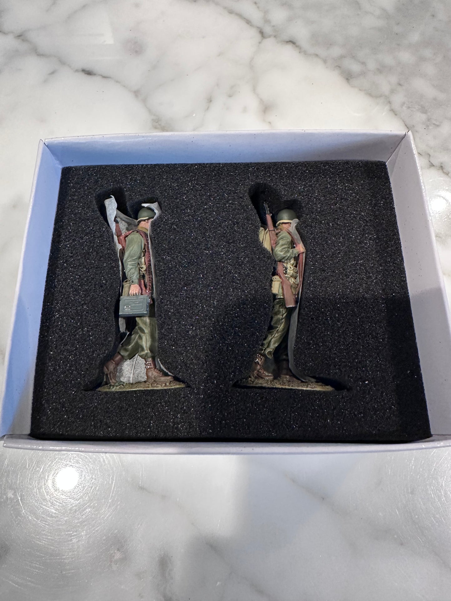 Two camouflage-patterned figurines in a box on a marble surface