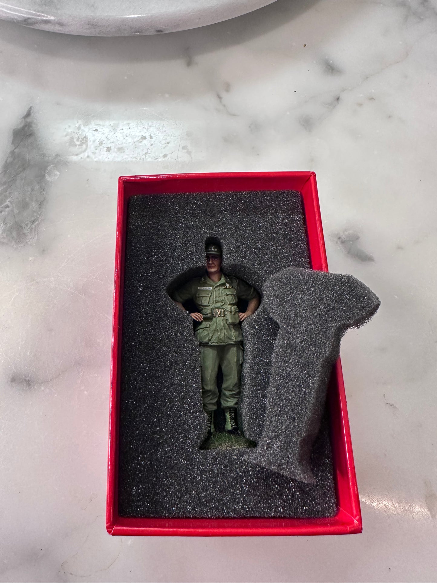 Model figure of a person in military uniform inside a red box on a marble surface