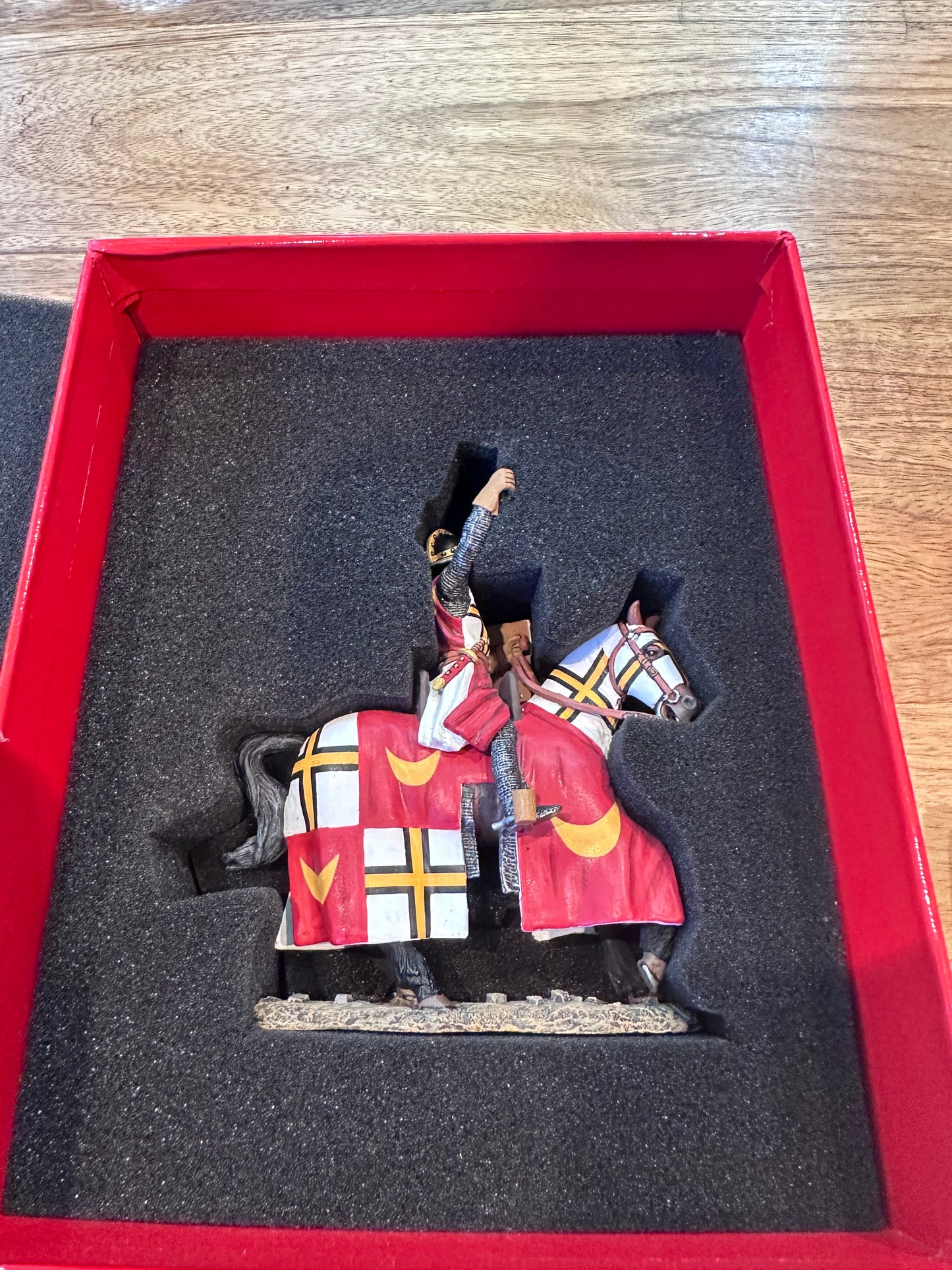 The Teutonic Flagbearer Toy Soldier Figurine with a red and white patterned outfit in a red box on a wooden surface