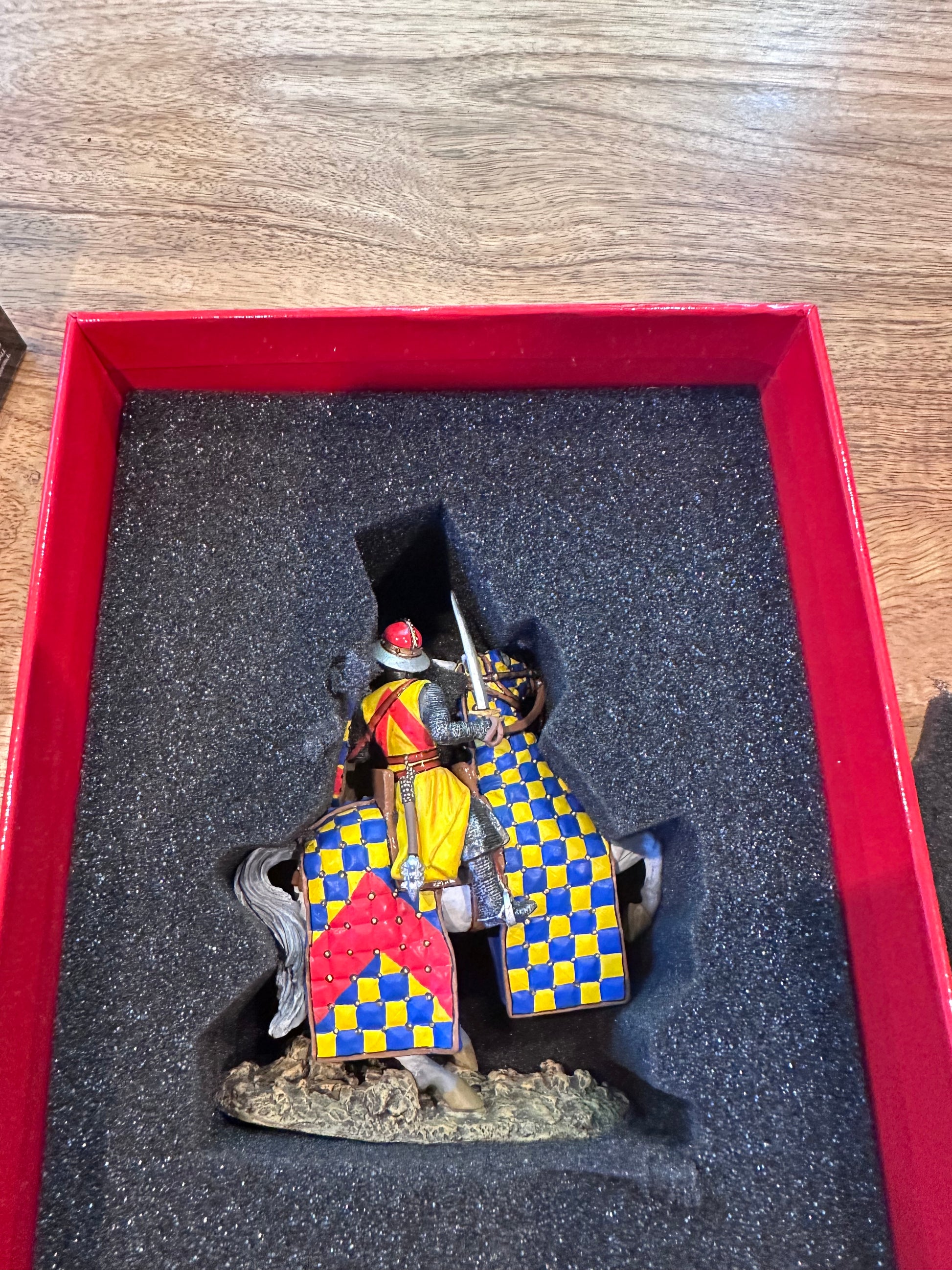Miniature figurine Robert de Chevron a knight with a colorful shield on a black cushioned tray.