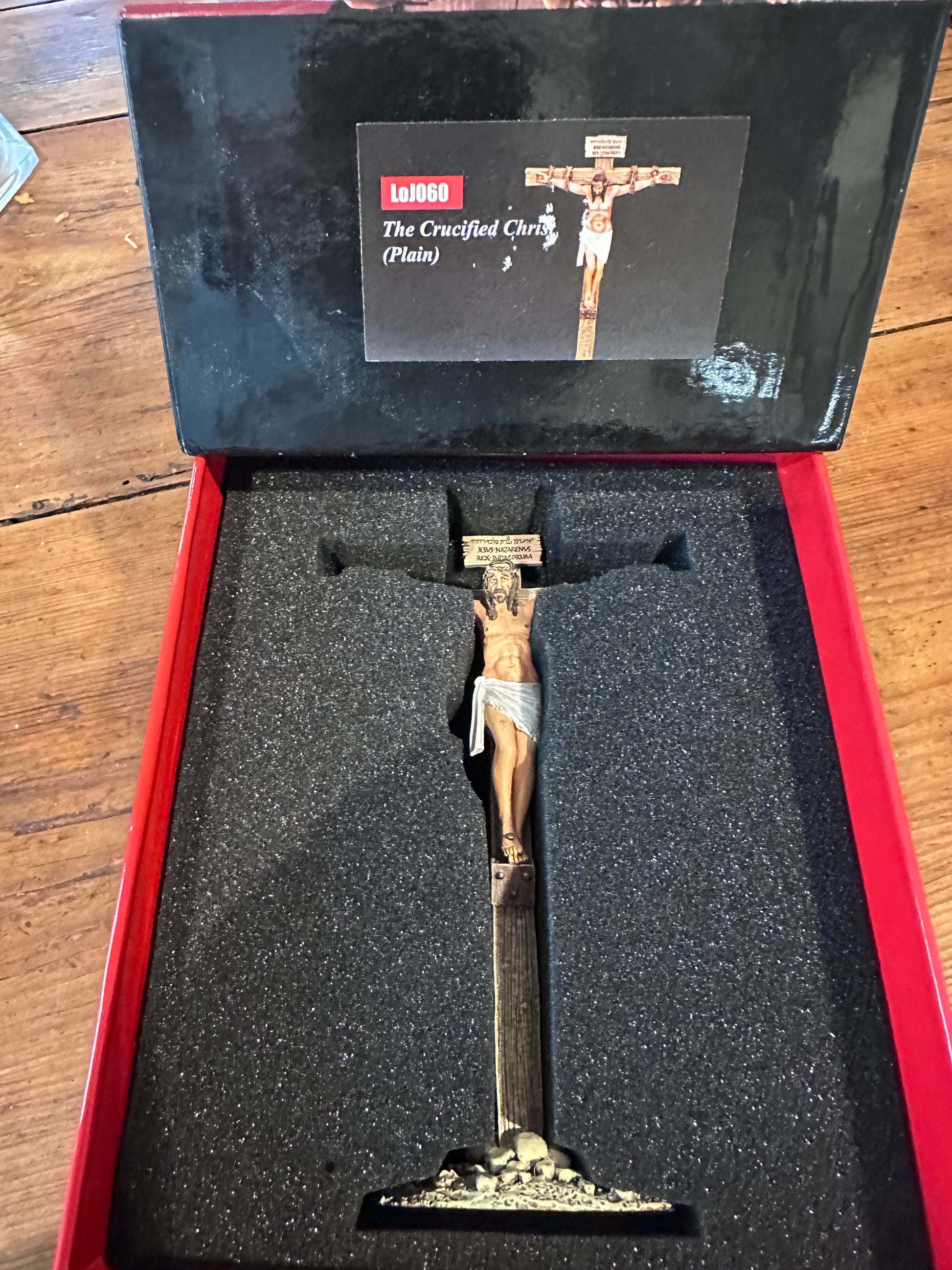 Statue of a crucified Christ figure in a display case with a brand label on a wooden surface.