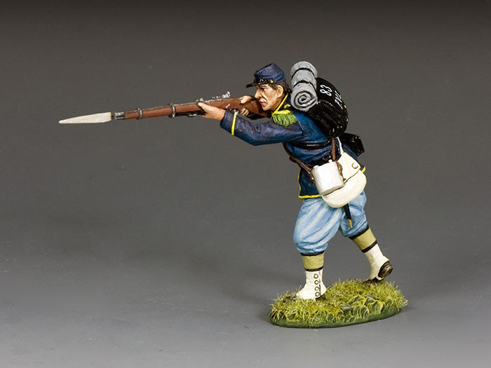 Miniature toy soldier figurine Union soldier advances while firing his musket, leaning forward with bayonet fixed and full campaign gear on his back.