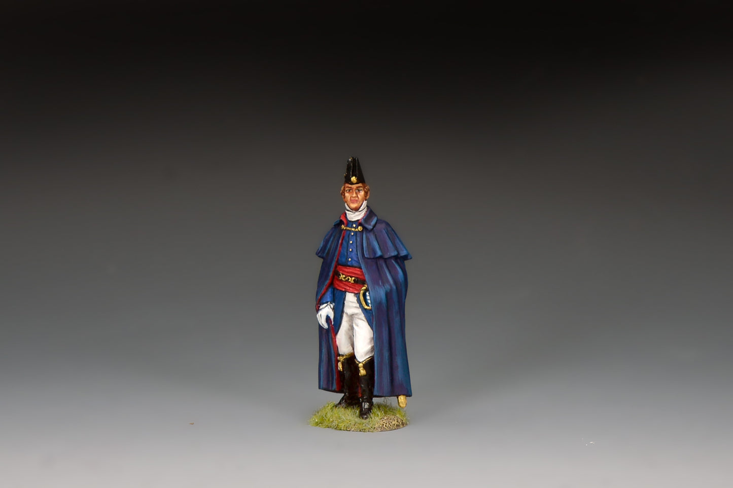King & Country matte-painted metal figure of the Duke of Wellington standing in a dark blue caped cloak and black cocked hat, red sash, holding a riding crop, on a groundwork base.
