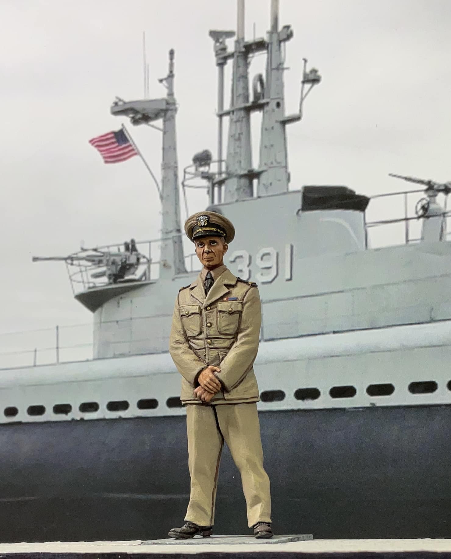 Person in military uniform standing in front of a ship with an American flag