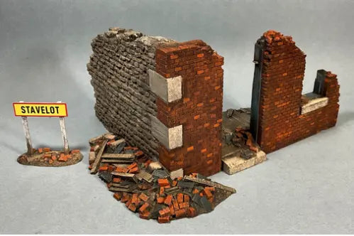 A model of a crumbling red brick wall and rubble, next to a small sign that reads STAVELOT on a gray surface. Diorama supplies for toy soldiers.