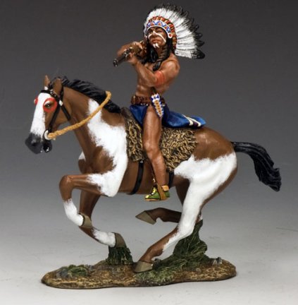 A painted figurine of a Native American warrior wearing a feathered headdress, riding a galloping brown and white horse, poised as if ready for action, set against a neutral background.