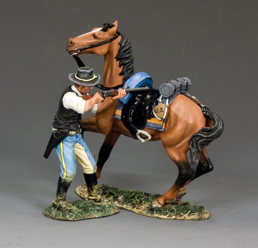 A painted military miniature figurine of a man in a black hat, vest, and blue-striped pants aiming a rifle while standing beside a brown horse equipped with a blue bedroll and black reins, both on a textured base.